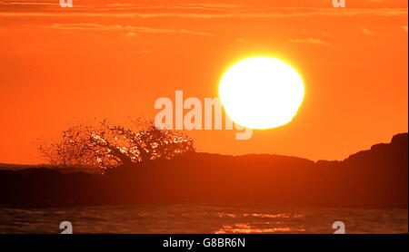 Waves crash over rocks at Cullercoats Bay, Tyne and Wear, as the sun rises. Stock Photo