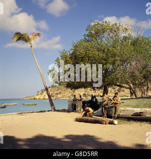 Royal Marines clean their weapons in the shade of a tree by the sunlit sea on Anguilla. British troops, as well as British Policeman, were sent to island following political unrest. The Island was bidding for independence from Great Britain. Stock Photo