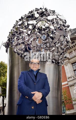 Contemporary Indian artist Subodh Gupta stands in front of his latest installation 'When Soak Becomes Spill', a six metre high stainless steel bucket overflowing with hundreds of pots, pans and cooking containers, which stands outside the Victoria and Albert Museum in Kensington, London. Stock Photo