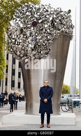 Contemporary Indian artist Subodh Gupta stands in front of his latest installation 'When Soak Becomes Spill', a six metre high stainless steel bucket overflowing with hundreds of pots, pans and cooking containers, which stands outside the Victoria and Albert Museum in Kensington, London. Stock Photo