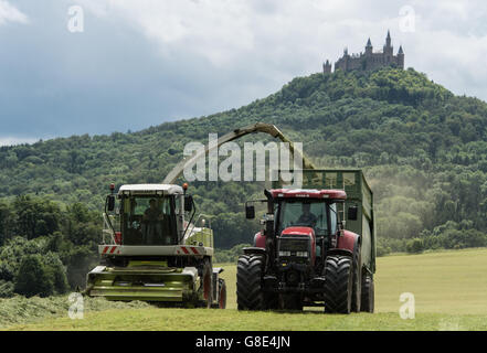 Bisingen, Germany. 28th June, 2016. A so-called grass harvester and a tractor harvest grass for livestock feeding, with Hohenzollern Castle pictured in the background, near Bisingen, Germany, 28 June 2016. Photo: PATRICK SEEGER/dpa/Alamy Live News Stock Photo