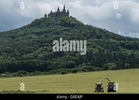 Bisingen, Germany. 28th June, 2016. A so-called grass harvester and a tractor harvest grass for livestock feeding, with Hohenzollern Castle pictured in the background, near Bisingen, Germany, 28 June 2016. Photo: PATRICK SEEGER/dpa/Alamy Live News Stock Photo