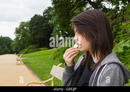 Young woman, adult or late teens, seated in park eating a slice of apple. Stock Photo