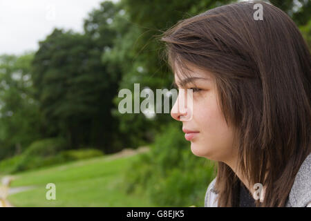 Young woman, adult or late teens, seated in park with a solemn or neutral expression on her face. Stock Photo