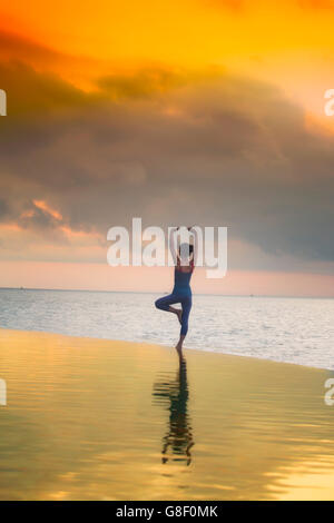 Yoga at dawn at an infinity pool - figure silhouetted against an orange sky Stock Photo