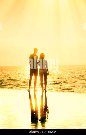 Honeymoon couple standing together at the edge of an infinity pool against a golden sunset/dawn Stock Photo