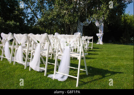Arch for wedding ceremony. White decorated chairs on a green lawn. Chairs set in rows for the wedding ceremony. Stock Photo