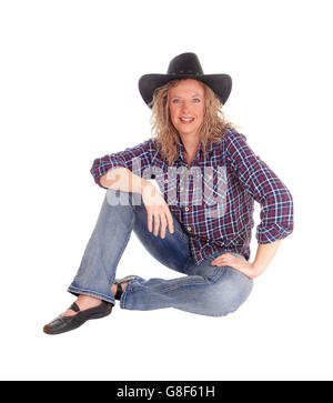 A nice middle age woman in jeans and with a black hat sitting on the floor, smiling, isolated for white background. Stock Photo