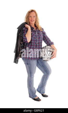 A middle age woman standing in jeans, holding her motorcycle helmet and leather jacket, isolated for white background. Stock Photo