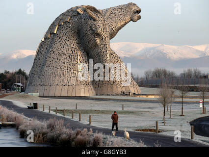 A dog walker passes the Kelpies in early morning sunshine on the Forth and Clyde canal near Falkirk, following heavy overnight frost across Central Scotland. Stock Photo