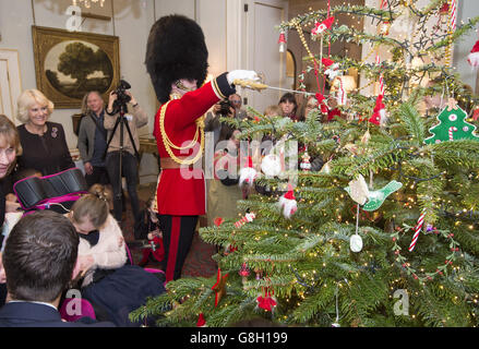 Captain Matt Wright of the Welsh Guards hangs a decoration with his sword as the Duchess of Cornwall (left) decorates the Clarence House Christmas tree with the help of children supported by Helen & Douglas House and The London Taxi Drivers' Fund for Underprivileged Children. Stock Photo