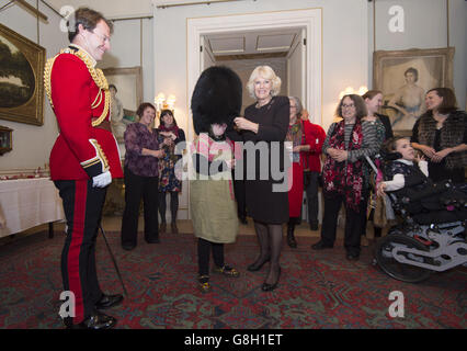 Alice Leigh tries on a bearskin hat belonging to Captain Matt Wright of the Welsh Guards (left) as the Duchess of Cornwall hosts an event to decorate the Clarence House Christmas tree with the help of children supported by Helen & Douglas House and The London Taxi Drivers' Fund for Underprivileged Children. Stock Photo