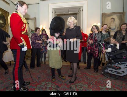 Alice Leigh tries on a bearskin hat belonging to Captain Matt Wright of the Welsh Guards (left) as the Duchess of Cornwall hosts an event to decorate the Clarence House Christmas tree with the help of children supported by Helen & Douglas House and The London Taxi Drivers' Fund for Underprivileged Children. Stock Photo