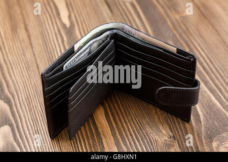 New black leather wallet with money over dark wooden background. Stock Photo