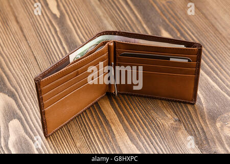 brown leather wallet with money over dark wooden background. Stock Photo