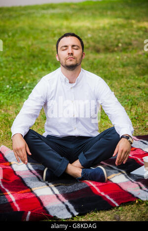 Man businessman meditating outdoors in lotus pose Stock Photo