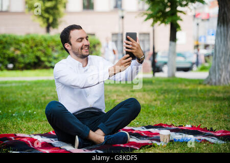 Modern young hispanic man taking a selfie at the park, with his tablet. Stock Photo