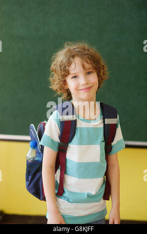 The pupil of elementary school stands in the class near a board. Behind shoulders at it a school backpack. The school student lo Stock Photo