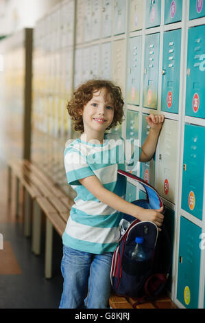 The primary school students standing in the hall near the lockers. The boy opened the backpack and something shifts.He has a pre Stock Photo