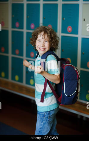 Elementary school student standing near lockers in school hallway. Behind kid's school backpack. Stock Photo