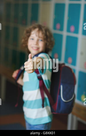 Elementary school student standing near lockers in school hallway. Behind kid's school backpack. The boy has blond curly hair an Stock Photo