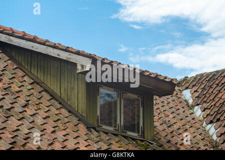 Mansard window in old tiled roof against blue sky Stock Photo