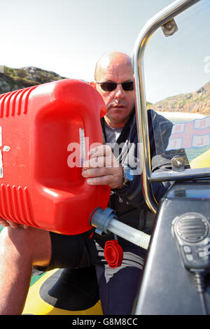 Man using a red plastic Jerry Can to fill up a RIB with petrol. Stock Photo