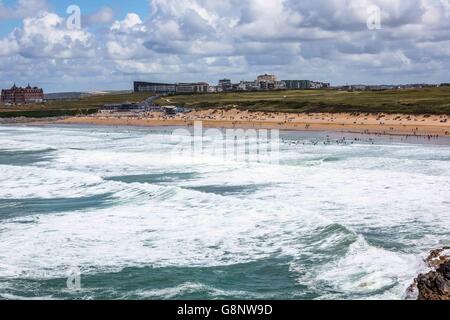 A crowd of people on the beach by the sea on Fistral Beach, Newquay, Cornwall, UK with the Headland Hotel behind