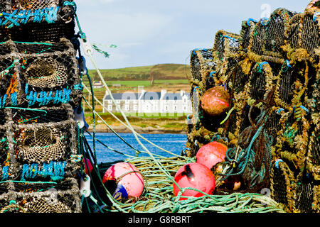Houses on Valentia Island seen through stacks of lobster and crab pots on the pier at Portmagee in County Kerry Ireland, Europe. Stock Photo