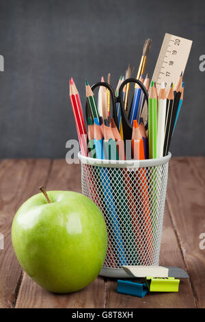 School and office supplies and apple on classroom table in front of blackboard Stock Photo