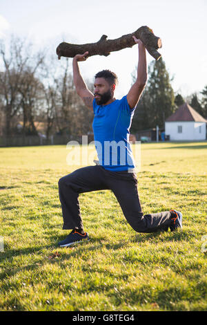 Young man doing squats with tree trunk on shoulder Stock Photo