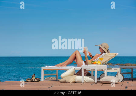 Woman with sun hat relaxes on beach terrace reading book Stock Photo