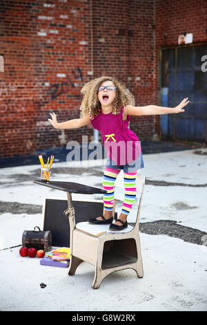 little girl stands on her chair while smiling in an outdoor, urban setting-back to school Stock Photo