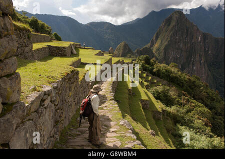 A lone hiker walking the path from the Sun Gate downhill towards the Inca site of Machu Picchu, Peru in late afternoon sunlight Stock Photo