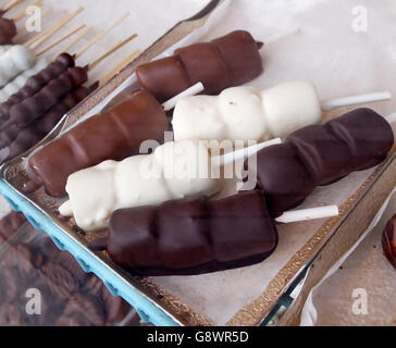 Marshmallow candy enrobed in dark chocolate, white chocolate, and milk chocolate, on sticks on a tray,  in a glass display case Stock Photo