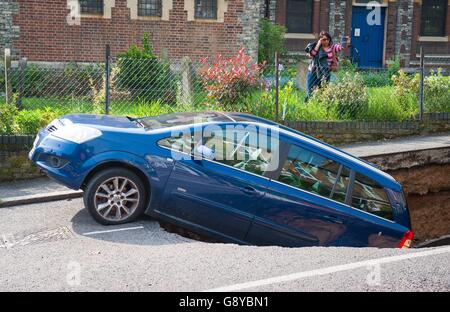 A woman takes a photograph of a car which has partially disappeared down a sinkhole in Woodland Terrace in Greenwich, south-east London.