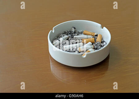 smoked cigarettes in white ashtray on wooden table Stock Photo