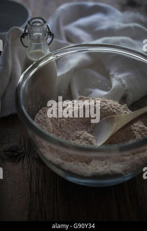 Flour in a glass mixing bowl and milk in a glass bottle on a rustic wooden table