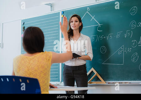 Teacher or docent or educator giving while lesson in front of a blackboard or board a sheet of paper and educate or teaching students or pupils or mates in a school or class Stock Photo