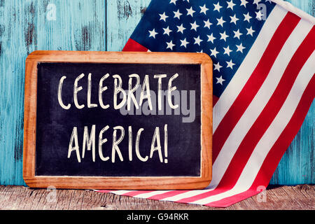 a wooden-framed chalkboard with the text celebrate America written in it and a flag of the United States, against a rustic blue Stock Photo