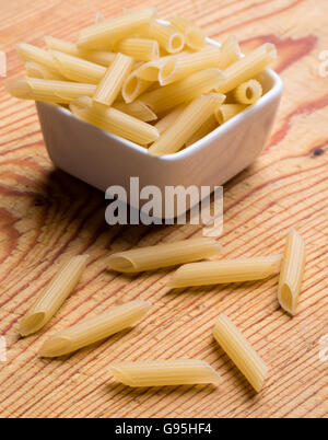 raw uncooked penne pasta in a white bowl on wooden table Stock Photo