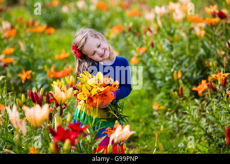 Cute little girl picking lily flowers in blooming summer garden. Child holding lilies bouquet in beautiful flower field. Stock Photo