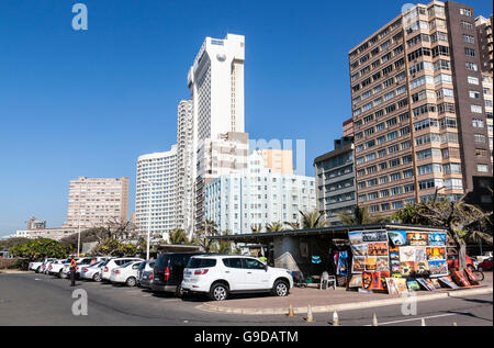 Motor vehicles parked next to street vendor against city skyline on Golden Mile beach front in Durban, South Africa Stock Photo