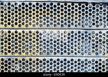 Blue stained and rusted rusted ventilation grill with many circular holes used as airflow for radiators on industrial machines a Stock Photo