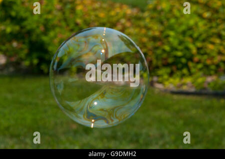 A soap bubble floats through the air in front of grass and trees. Stock Photo