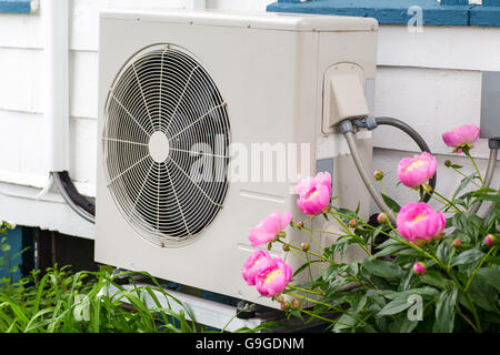 Air conditioning/ Heat pump unit on the side of a home among the flowers. Stock Photo