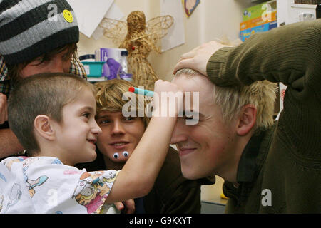 Regan Gibbs, age 5, from the Shetland Islands (centre), draws a smiley face on the forehead of Tom Fletcher (right), as he visits Great Ormond Street Children's Hospital with his fellow bandmates in McFly (left to right) Danny Jones and Dougie Poynter. Stock Photo
