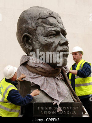 PHOTO. A pair of engineers uncover a bronze statue of Nelson Mandela, the former President of South Africa, after it was returned to its position next to the Royal Festival Hall. It was removed due to building work at the Hall on the South Bank in Central London. The statue was lifted into place in front of the Royal Festival Hall in preparation for the re-opening of the hall in June. Stock Photo