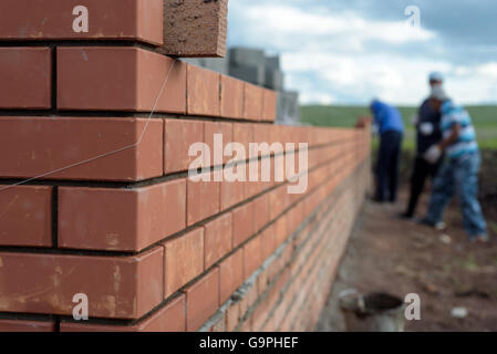 Newly built red brick wall of a newly built house with bricklayers in the background Stock Photo