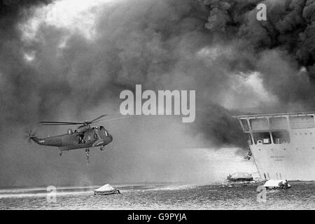 A Royal Navy Sea King helicopter hovers over life-rafts to pick up survivors from the blazing British landing ship, RFA Sir Galahad, during the devastating air attack on Sir Galahad and Sir Tristram. Stock Photo